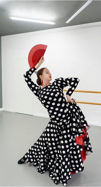 Fotografía de mujer bailando flamenco con abanico rojo en la mano derecha.